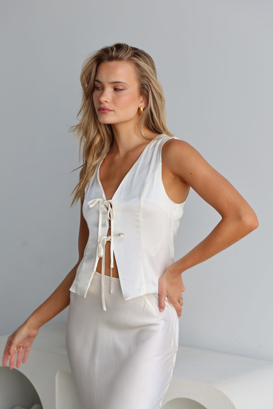 A woman wearing a white satin vest with a tie front and V-neck, sleeveless vest-style design.