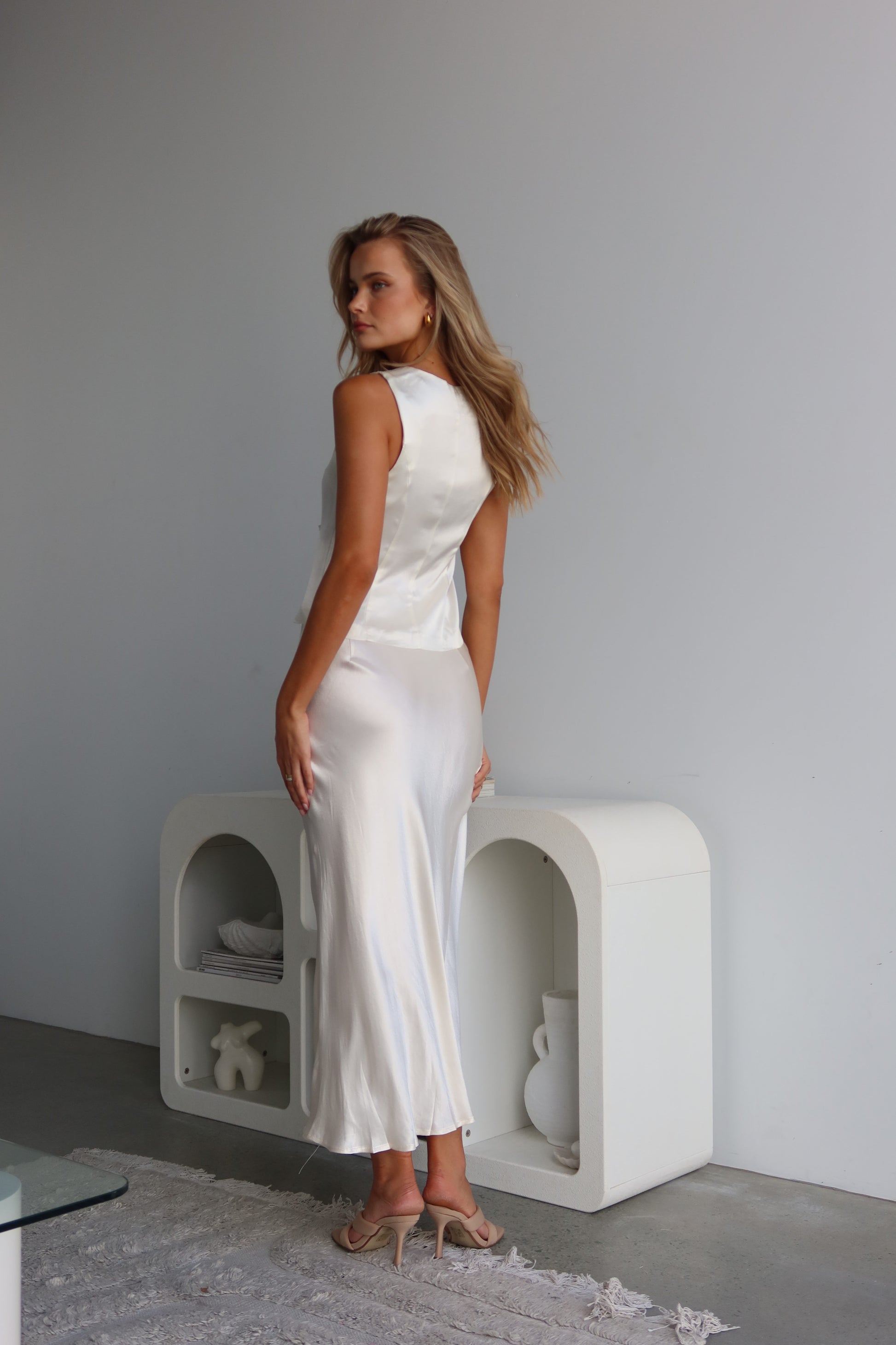 A woman wearing a white satin vest with a tie front and V-neck, sleeveless vest-style design.