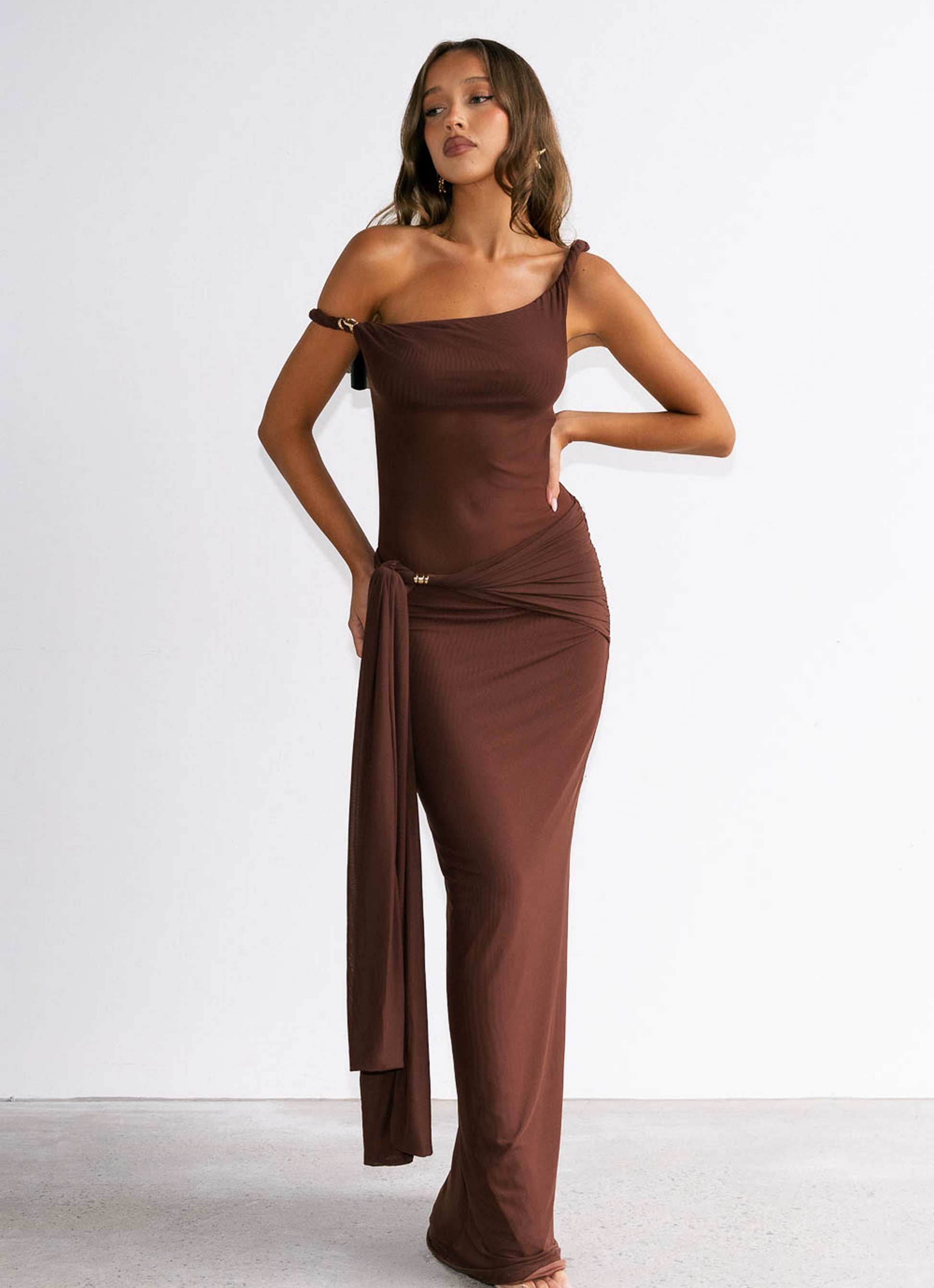Woman wearing a brown one-shoulder dress against a white background