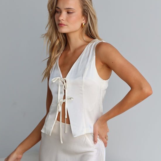 A woman wearing a white satin vest with a tie front and V-neck, sleeveless vest-style design.