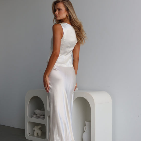 A woman wearing a white satin vest with a tie front and V-neck, sleeveless vest-style design.