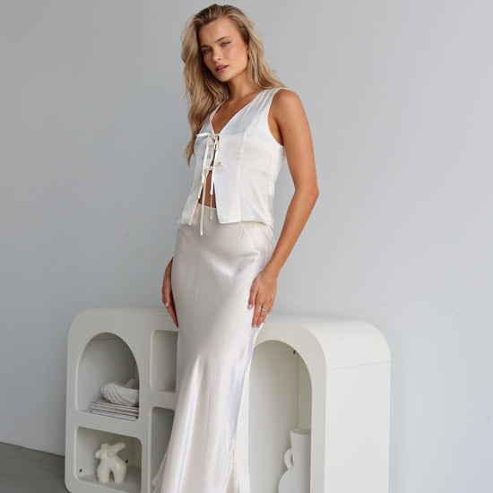A woman wearing a white satin vest with a tie front and V-neck, sleeveless vest-style design.