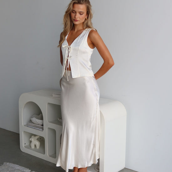 A woman wearing a white satin vest with a tie front and V-neck, sleeveless vest-style design.